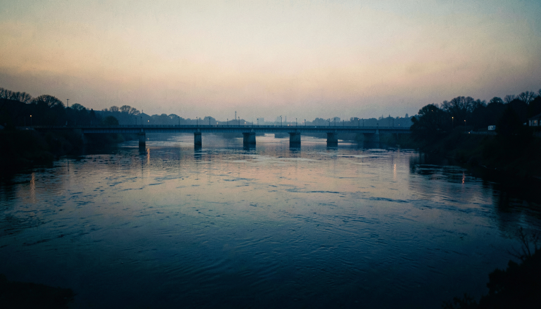 Wide cinematic view of three rivers meeting at dawn, soft amber light on water, muted blue bridge silhouettes, gentle haze over the horizon, shallow depth of field