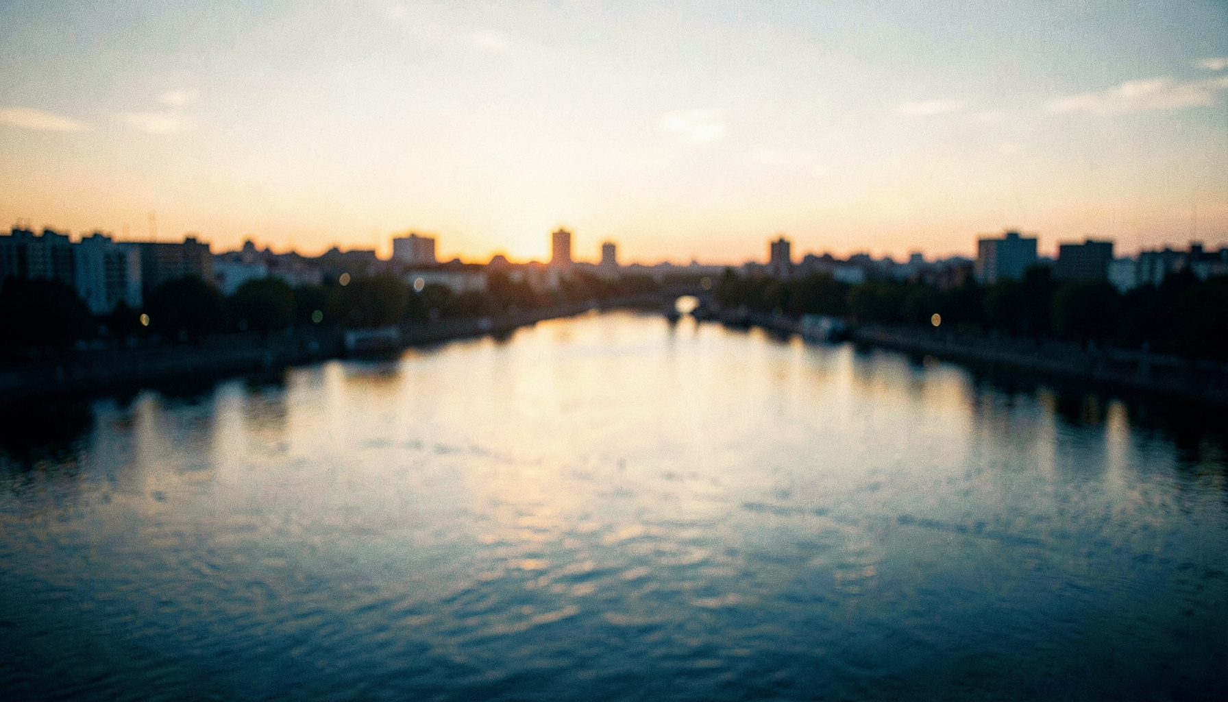 Wide cinematic view of three rivers meeting under a soft golden sunset, with blurred city silhouettes and a warm civic mood in amber and slate blue tones