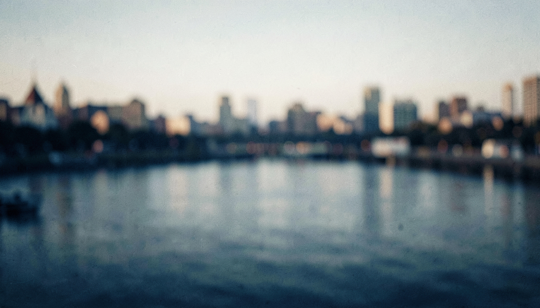 Soft-focus panoramic riverfront scene at dawn, muted blue and warm beige tones, quiet civic atmosphere with blurred skyline