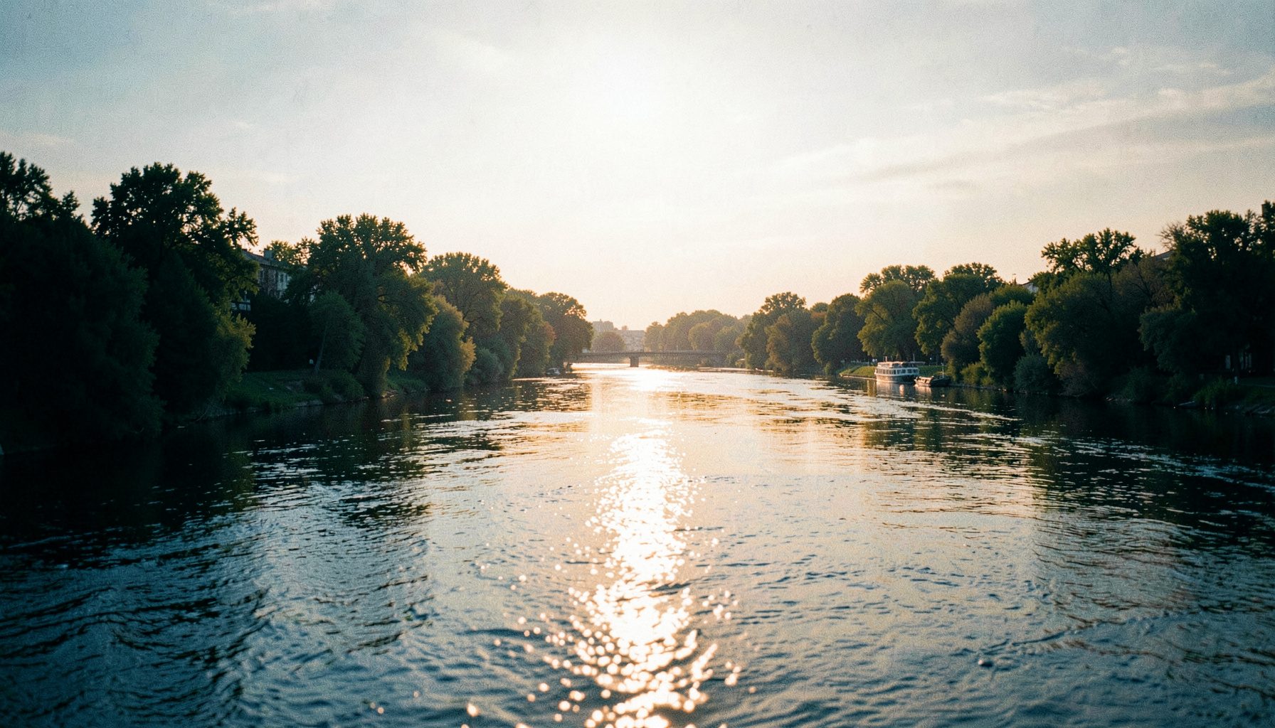 Soft golden-hour light reflecting off a wide river with tree-lined banks in muted greens and warm amber tones, conveying a calm civic atmosphere.